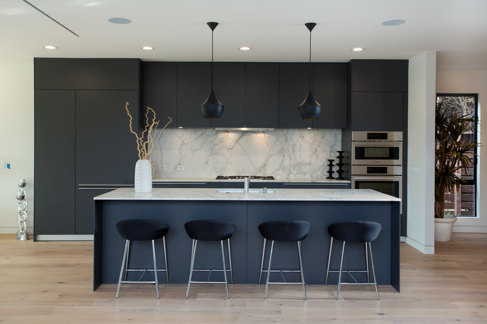 Large modern single-wall kitchen/diner in Los Angeles with a submerged sink, flat-panel cabinets, grey cabinets, marble worktops, white splashback, marble splashback, stainless steel appliances, light hardwood flooring, an island and white worktops.