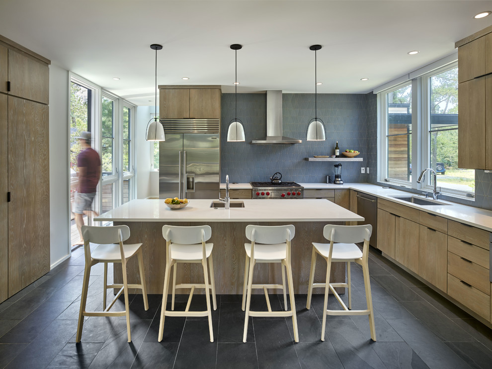Small minimalist l-shaped slate floor and black floor open concept kitchen photo in Other with an undermount sink, flat-panel cabinets, light wood cabinets, solid surface countertops, gray backsplash, ceramic backsplash, stainless steel appliances and an island