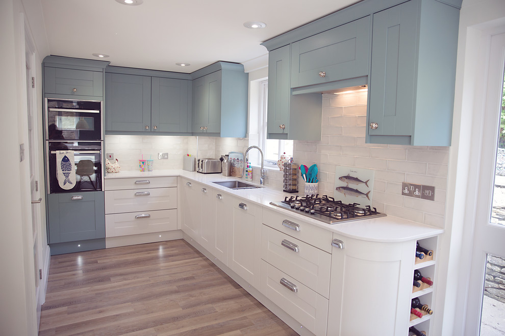 Kleine Maritime Küche ohne Insel in L-Form mit Doppelwaschbecken, Schrankfronten im Shaker-Stil, blauen Schränken, Küchenrückwand in Weiß, Küchengeräten aus Edelstahl und weißer Arbeitsplatte in Cornwall