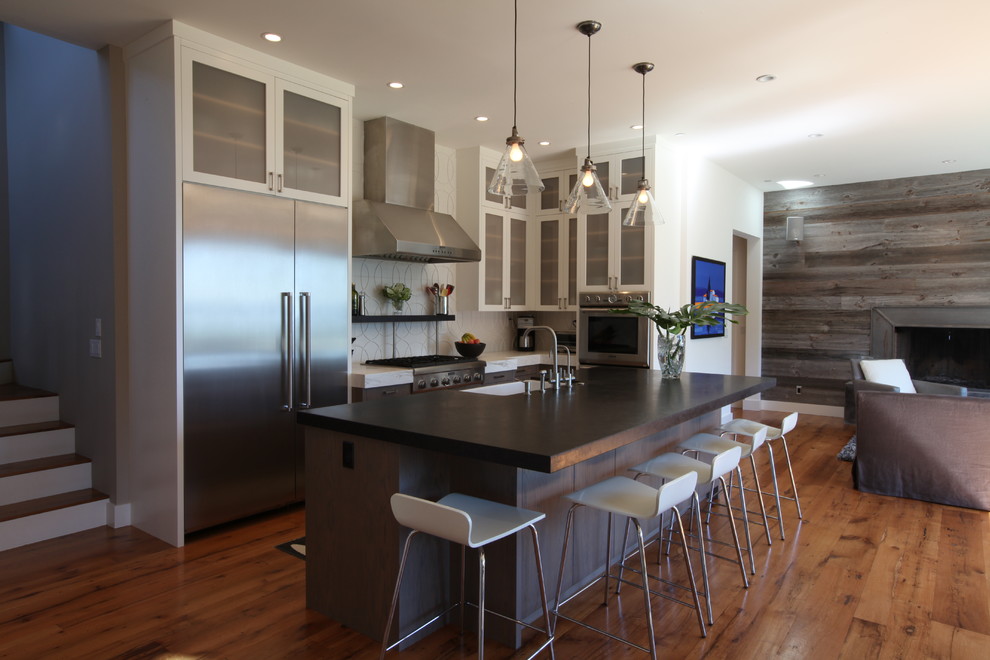 Inspiration for a mid-sized coastal l-shaped medium tone wood floor eat-in kitchen remodel in San Francisco with an undermount sink, glass-front cabinets, gray cabinets, granite countertops, white backsplash, ceramic backsplash, stainless steel appliances and an island