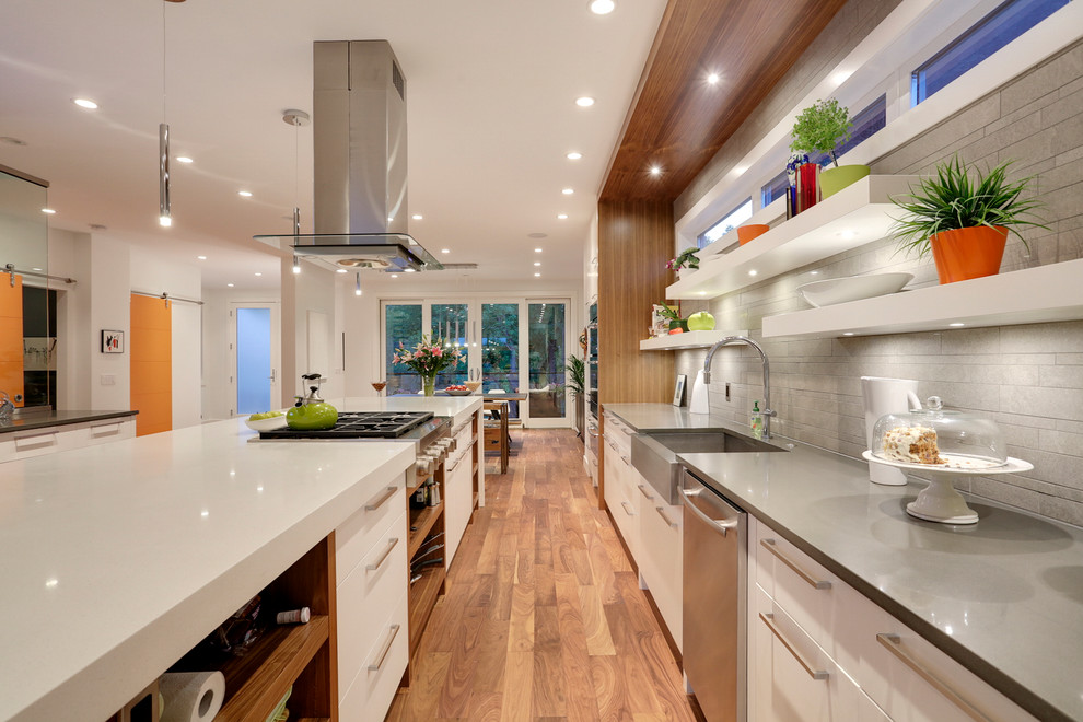 Offene, Zweizeilige Moderne Küche mit Landhausspüle, flächenbündigen Schrankfronten, weißen Schränken, Küchenrückwand in Grau, Küchengeräten aus Edelstahl, braunem Holzboden und Kücheninsel in Calgary