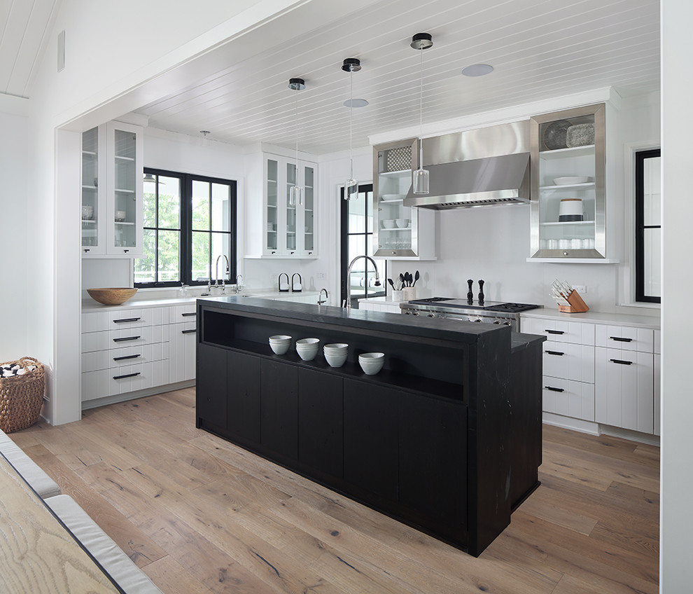 Idéer för lantliga grått kök med öppen planlösning, med luckor med glaspanel, skåp i rostfritt stål, vitt stänkskydd, rostfria vitvaror, ljust trägolv och en köksö