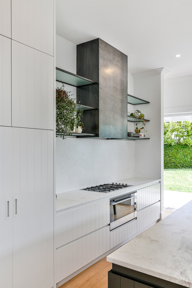Inspiration for a mid-sized timeless galley light wood floor and brown floor open concept kitchen remodel in Auckland with a drop-in sink, white cabinets, marble countertops, white backsplash, marble backsplash, black appliances, an island and white countertops