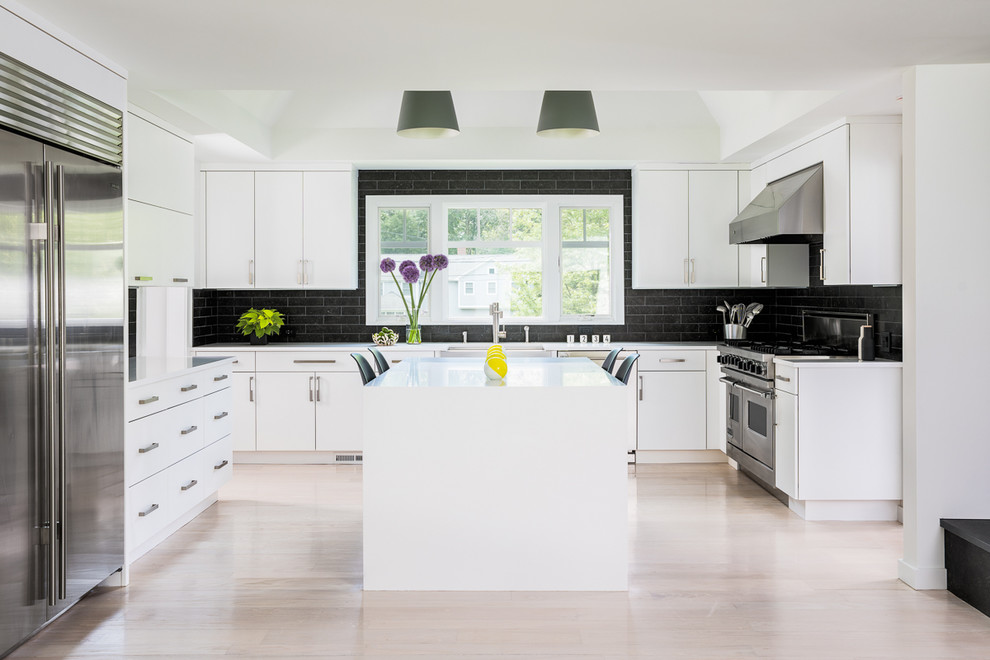 Eat-in kitchen - large modern u-shaped light wood floor and beige floor eat-in kitchen idea in New York with a farmhouse sink, flat-panel cabinets, white cabinets, quartz countertops, black backsplash, ceramic backsplash, stainless steel appliances, an island and white countertops