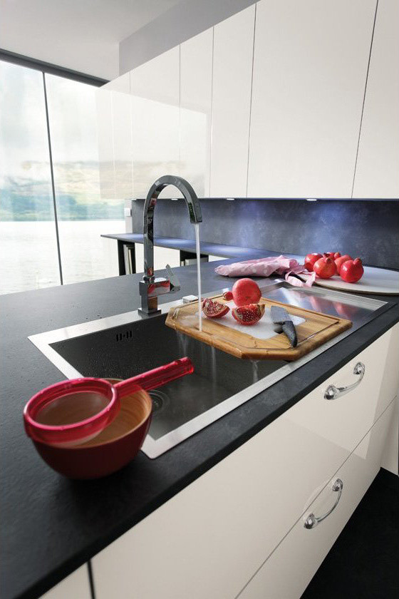 Cette image montre une grande cuisine ouverte minimaliste en U avec un placard à porte plane, des portes de placard blanches, une crédence noire, un électroménager en acier inoxydable et un sol gris.
