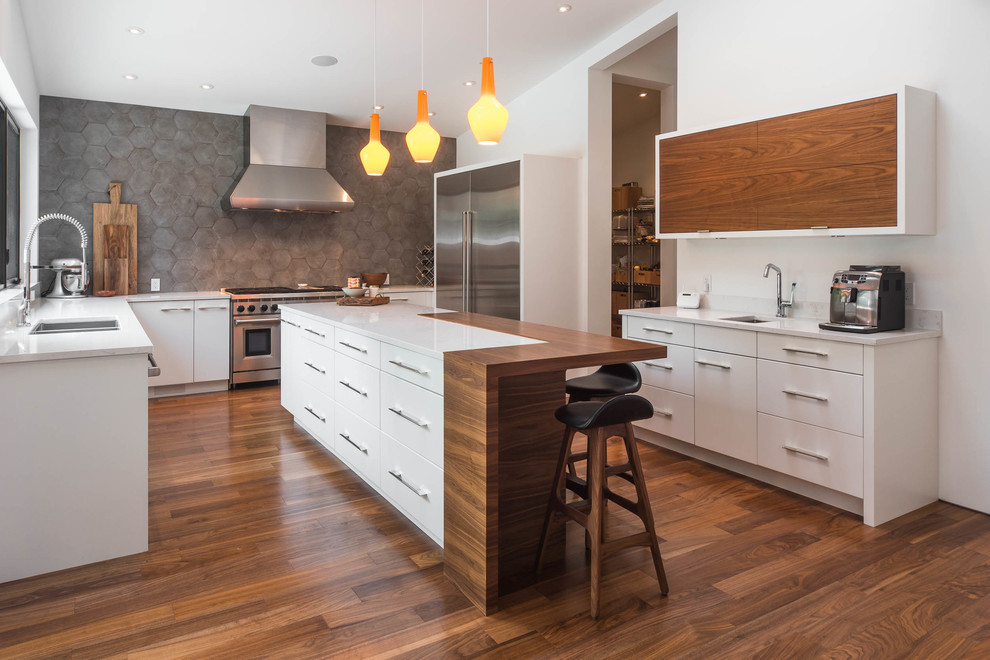 Retro Küche mit Doppelwaschbecken, flächenbündigen Schrankfronten, weißen Schränken, Küchenrückwand in Grau, Küchengeräten aus Edelstahl, braunem Holzboden und Kücheninsel in Vancouver