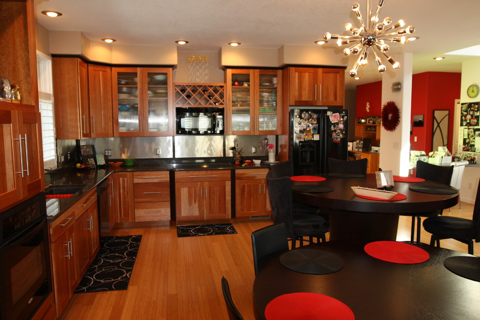 Example of a mid-sized trendy l-shaped eat-in kitchen design in Denver with a drop-in sink, flat-panel cabinets, medium tone wood cabinets, granite countertops, metallic backsplash, black appliances and no island