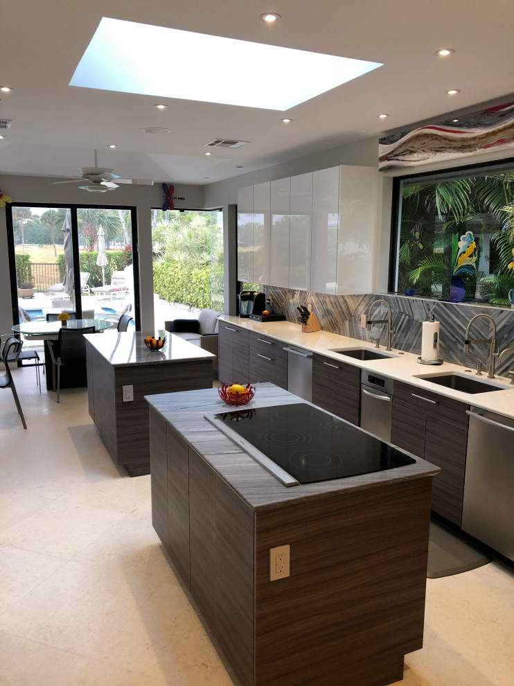 This is an example of a large modern galley enclosed kitchen in Miami with a submerged sink, flat-panel cabinets, porcelain splashback, stainless steel appliances, limestone flooring, multiple islands and beige floors.