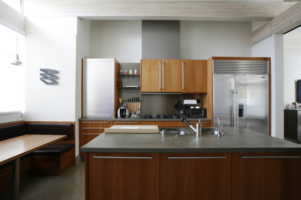 Bild på ett mellanstort funkis kök, med en undermonterad diskho, släta luckor, skåp i mellenmörkt trä, bänkskiva i betong, grått stänkskydd, rostfria vitvaror, linoleumgolv och en köksö