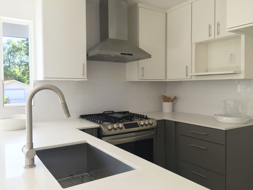 This is an example of a small modern u-shaped open plan kitchen in Austin with a single-bowl sink, flat-panel cabinets, grey cabinets, composite countertops, white splashback, metro tiled splashback, stainless steel appliances, concrete flooring and a breakfast bar.