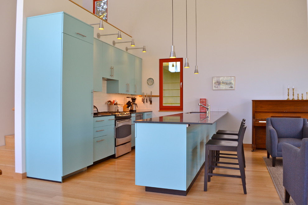 Mid-sized trendy galley medium tone wood floor open concept kitchen photo in Seattle with flat-panel cabinets, blue cabinets, white backsplash, subway tile backsplash, paneled appliances, an undermount sink and a peninsula