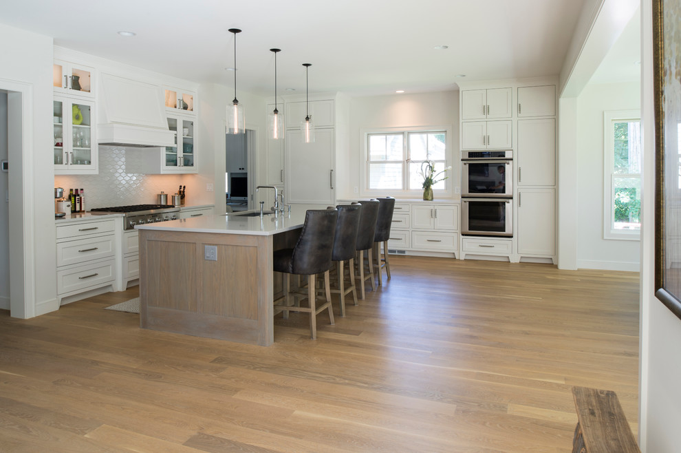 Beach style l-shaped light wood floor eat-in kitchen photo in Minneapolis with white cabinets, white backsplash and an island