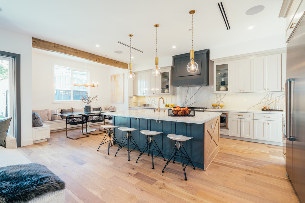 Inspiration for a coastal light wood floor and beige floor open concept kitchen remodel in Los Angeles with shaker cabinets, white cabinets, white backsplash, stone slab backsplash, stainless steel appliances, an island and white countertops