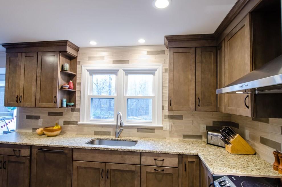 Bild på ett mellanstort amerikanskt kök, med en undermonterad diskho, luckor med infälld panel, bruna skåp, granitbänkskiva, beige stänkskydd, stänkskydd i sten, rostfria vitvaror, ljust trägolv och en köksö