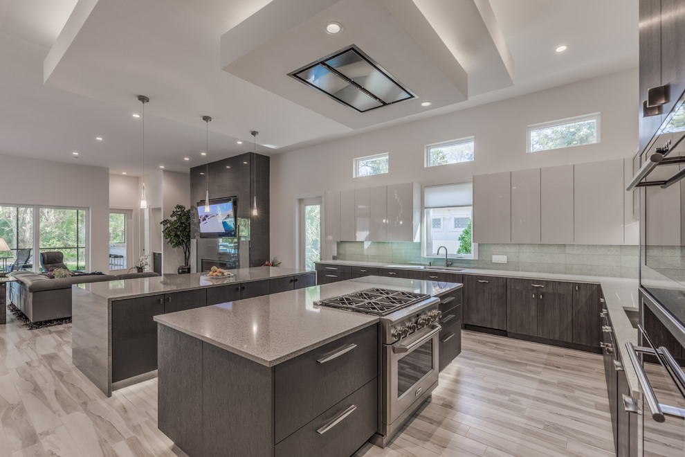 Photo of a large contemporary l-shaped kitchen/diner in Jacksonville with a submerged sink, flat-panel cabinets, white cabinets, engineered stone countertops, blue splashback, glass tiled splashback, stainless steel appliances, porcelain flooring, multiple islands, grey floors and grey worktops.
