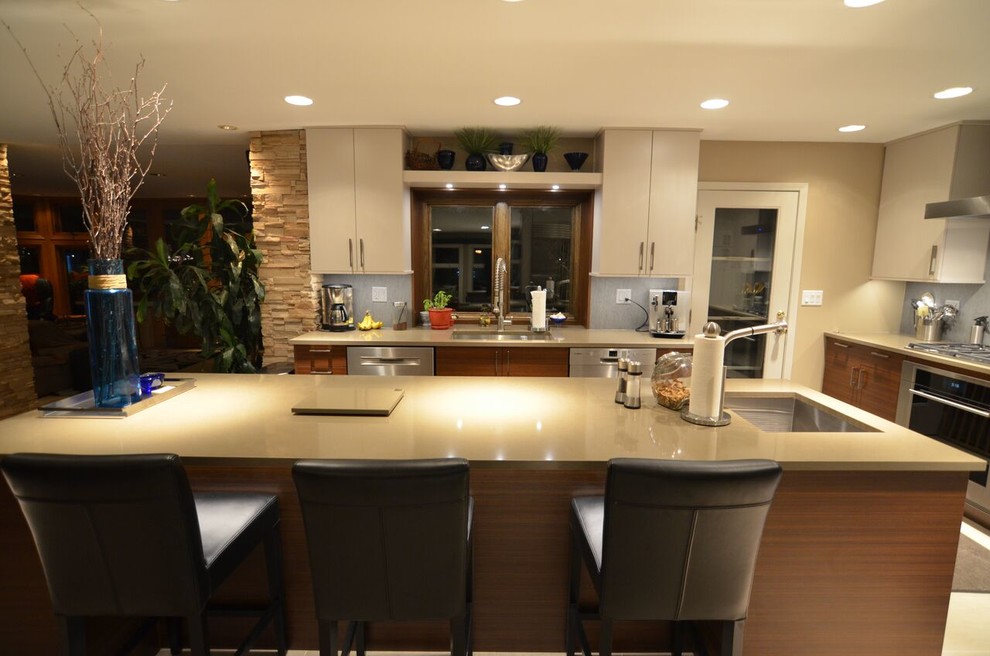 Foto på ett stort kök, med en undermonterad diskho, släta luckor, vita skåp, blått stänkskydd, rostfria vitvaror och en köksö
