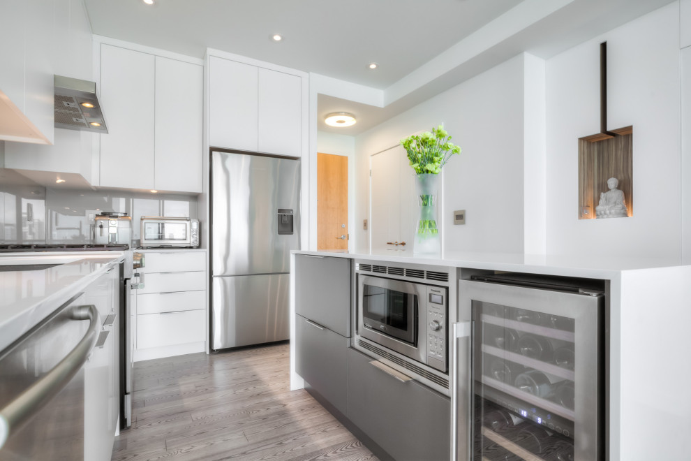 Photo of a small modern galley kitchen/diner in Toronto with a submerged sink, flat-panel cabinets, white cabinets, engineered stone countertops, grey splashback, glass sheet splashback, stainless steel appliances, medium hardwood flooring, an island, grey floors, white worktops and a coffered ceiling.