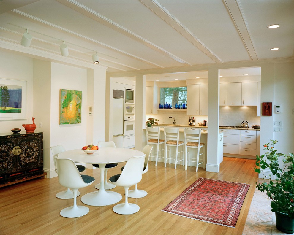 Eat-in kitchen - small contemporary galley light wood floor and beige floor eat-in kitchen idea in Boston with flat-panel cabinets, white cabinets, white appliances, granite countertops, white backsplash, a peninsula and beige countertops