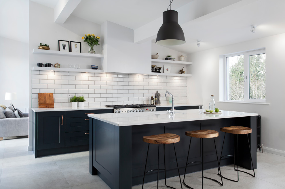 Classic galley kitchen in Belfast with a single-bowl sink, stainless steel appliances, an island, shaker cabinets, blue cabinets, white splashback, metro tiled splashback, grey floors and white worktops.