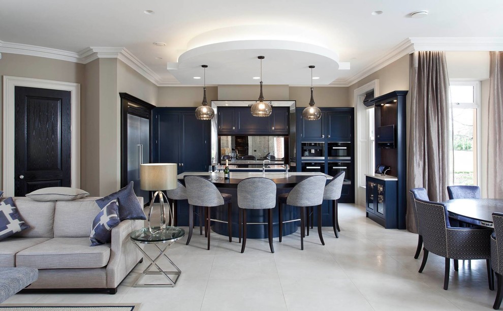 На фото: п-образная кухня-гостиная в стиле неоклассика (современная классика) с фасадами с утопленной филенкой, синими фасадами, зеркальным фартуком, черной техникой, островом и белым полом