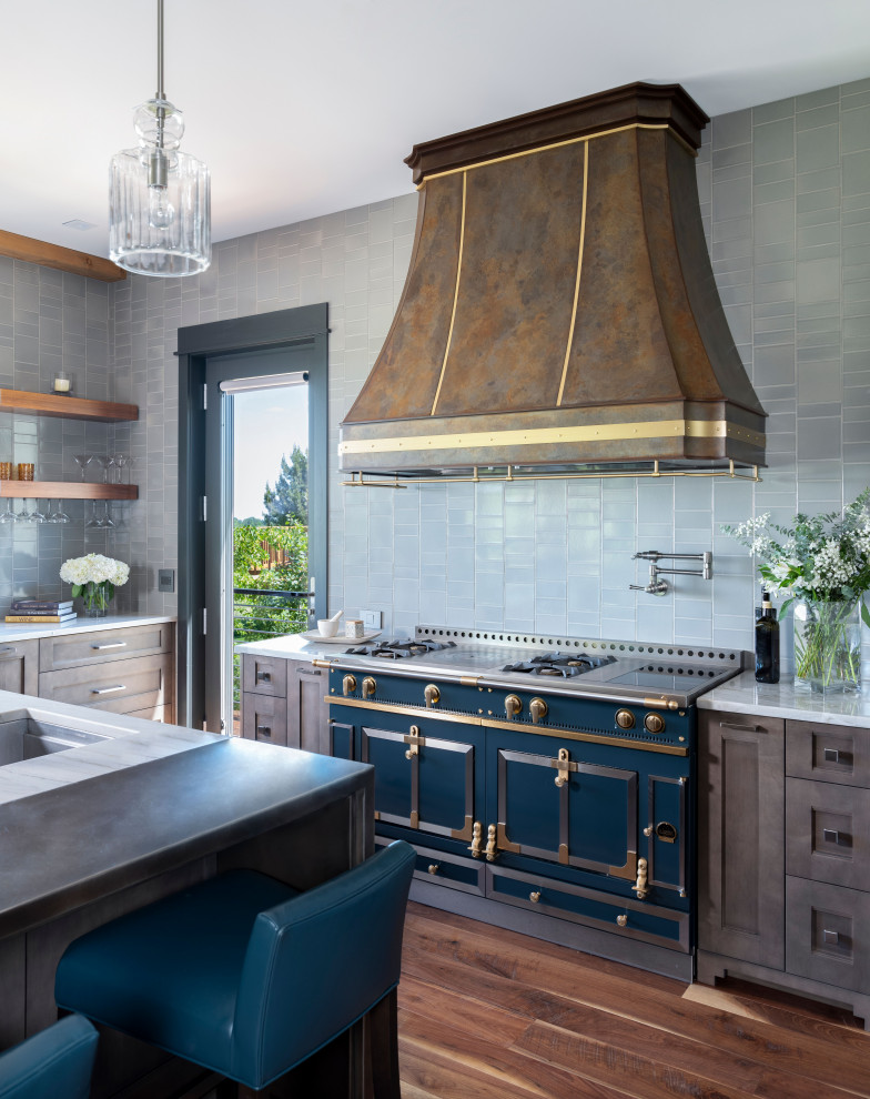 Example of a mid-sized minimalist medium tone wood floor and exposed beam eat-in kitchen design in Other with a farmhouse sink, shaker cabinets, gray backsplash, porcelain backsplash, colored appliances and an island