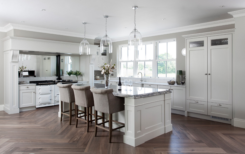 Klassisk inredning av ett mellanstort grå grått l-kök, med en köksö, en dubbel diskho, grå skåp, spegel som stänkskydd, vita vitvaror, mörkt trägolv, brunt golv och skåp i shakerstil