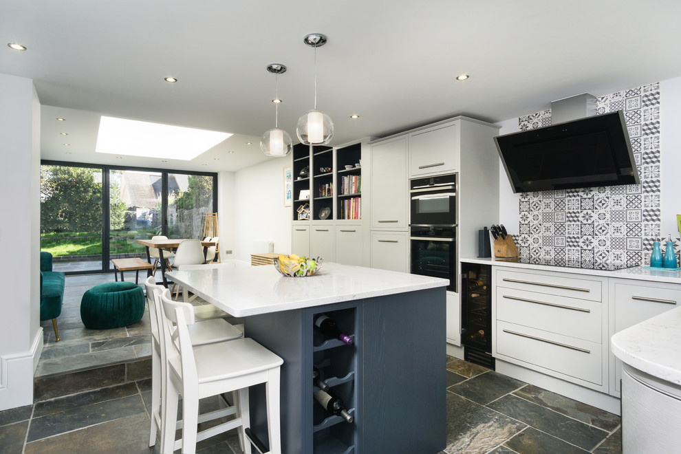 Contemporary l-shaped kitchen/diner in Other with flat-panel cabinets, white cabinets, black appliances, an island, grey floors, white worktops and multi-coloured splashback.