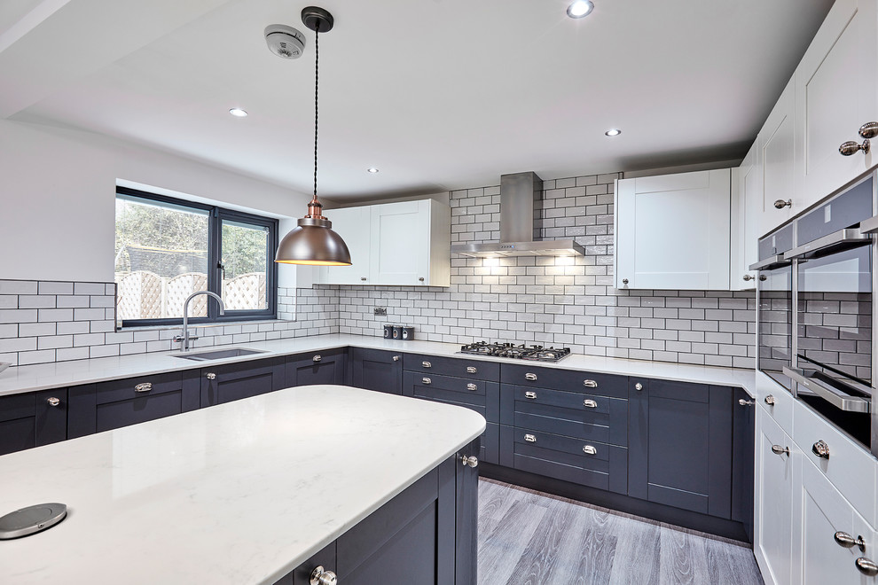 This is an example of a medium sized classic u-shaped kitchen/diner in Other with an integrated sink, shaker cabinets, grey cabinets, quartz worktops, white splashback, porcelain splashback, black appliances, laminate floors, an island, grey floors and white worktops.