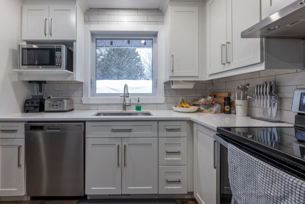 Foto på ett mellanstort funkis vit kök, med en enkel diskho, skåp i shakerstil, vita skåp, bänkskiva i kvarts, vitt stänkskydd, stänkskydd i keramik, rostfria vitvaror, vinylgolv och brunt golv