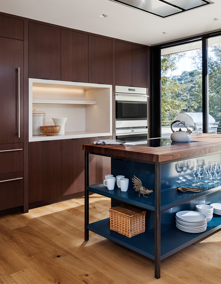 Example of a trendy light wood floor and beige floor kitchen design in San Francisco with flat-panel cabinets, dark wood cabinets, wood countertops, stainless steel appliances and an island