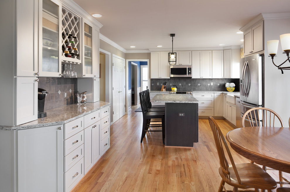 Mid-sized transitional l-shaped medium tone wood floor eat-in kitchen photo in DC Metro with a farmhouse sink, recessed-panel cabinets, white cabinets, quartz countertops, gray backsplash, porcelain backsplash, stainless steel appliances and an island