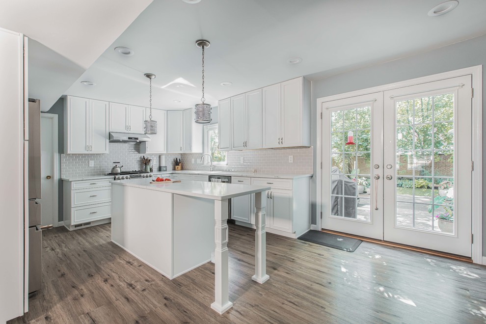 Large contemporary u-shaped open plan kitchen in DC Metro with a submerged sink, raised-panel cabinets, white cabinets, engineered stone countertops, grey splashback, metro tiled splashback, stainless steel appliances, vinyl flooring, an island, brown floors and white worktops.