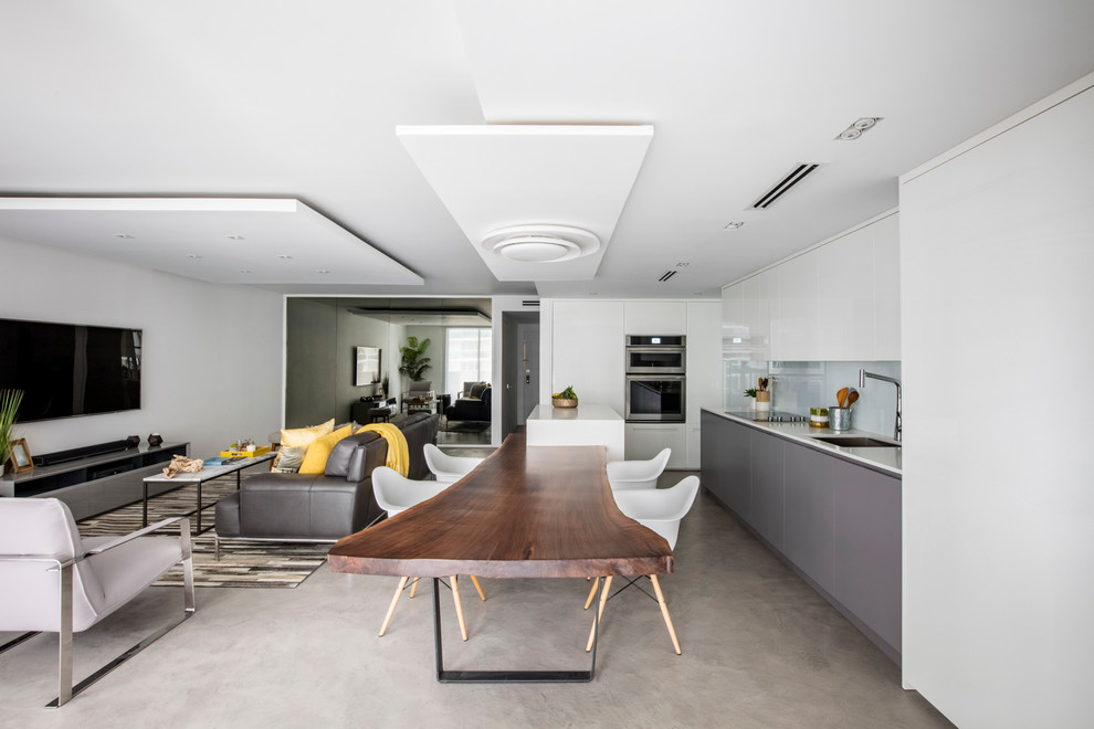 Photo of a medium sized contemporary l-shaped open plan kitchen in Miami with a submerged sink, flat-panel cabinets, white cabinets, engineered stone countertops, white splashback, glass sheet splashback, integrated appliances, concrete flooring and an island.