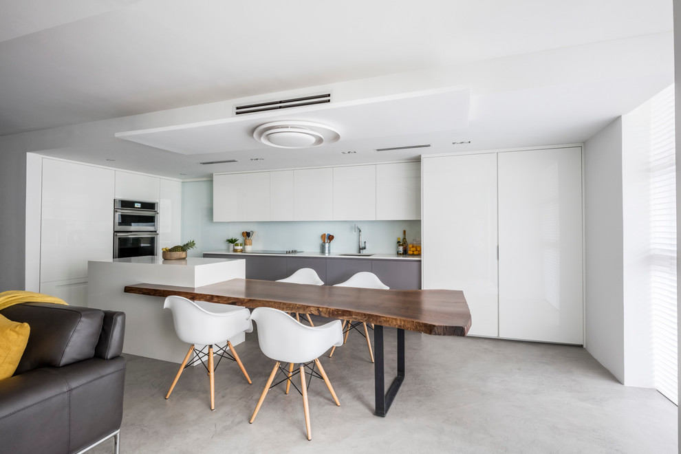 This is an example of a medium sized contemporary l-shaped kitchen/diner in Miami with a submerged sink, flat-panel cabinets, white cabinets, engineered stone countertops, white splashback, glass sheet splashback, integrated appliances, concrete flooring and an island.