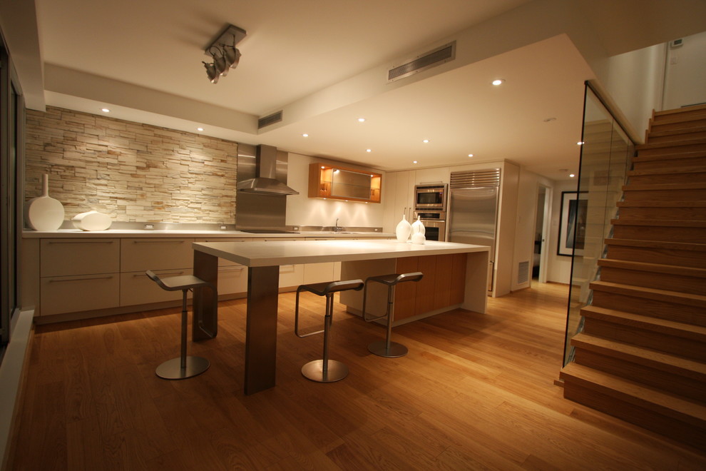 This is an example of a large contemporary l-shaped enclosed kitchen in Toronto with a submerged sink, flat-panel cabinets, white cabinets, composite countertops, metallic splashback, metal splashback, stainless steel appliances, light hardwood flooring, an island and brown floors.