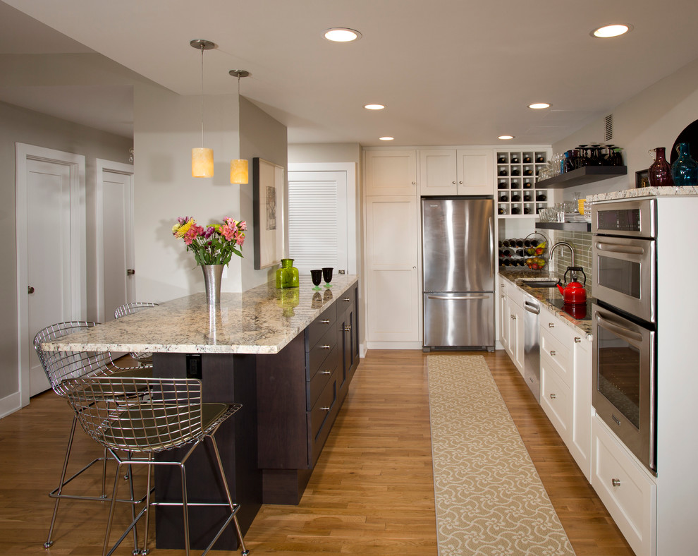 Example of a mid-sized trendy galley light wood floor open concept kitchen design in DC Metro with an undermount sink, shaker cabinets, white cabinets, granite countertops, gray backsplash, glass tile backsplash, stainless steel appliances and a peninsula