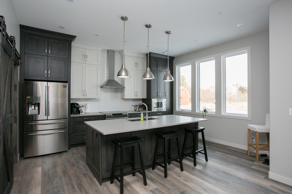 Medium sized contemporary single-wall open plan kitchen in Calgary with a submerged sink, shaker cabinets, dark wood cabinets, composite countertops, white splashback, metro tiled splashback, stainless steel appliances, medium hardwood flooring and an island.