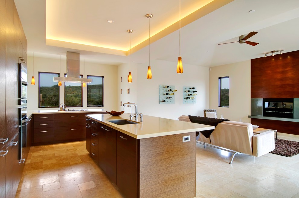 Photo of a large modern galley open plan kitchen in San Francisco with a submerged sink, flat-panel cabinets, dark wood cabinets, engineered stone countertops, white splashback, glass tiled splashback, stainless steel appliances, travertine flooring, an island, beige floors and white worktops.