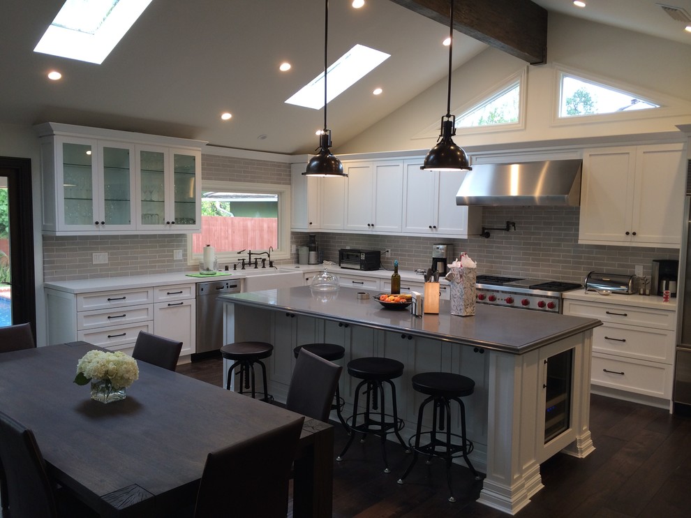 Inspiration for a modern l-shaped dark wood floor eat-in kitchen remodel in Los Angeles with a farmhouse sink, shaker cabinets, white cabinets, quartzite countertops, gray backsplash, ceramic backsplash, stainless steel appliances and an island