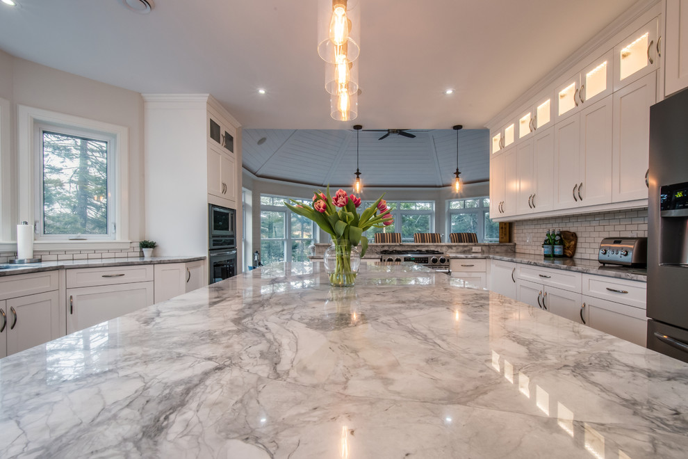 Large contemporary kitchen/diner in Other with a submerged sink, shaker cabinets, white cabinets, marble worktops, white splashback, metro tiled splashback, stainless steel appliances, medium hardwood flooring and an island.