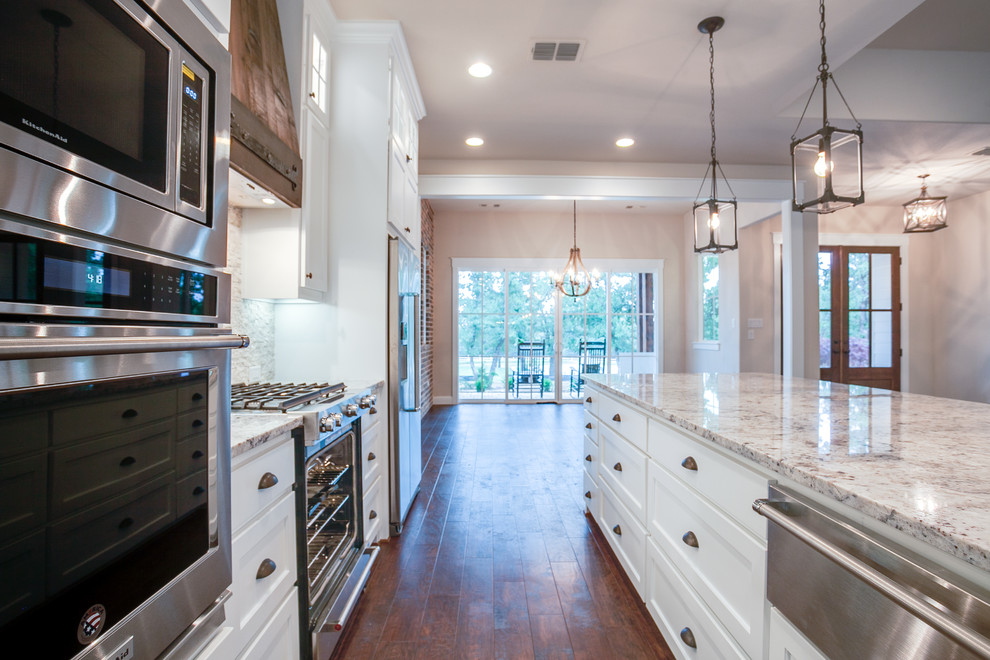 Foto på ett stort lantligt kök, med en rustik diskho, skåp i shakerstil, vita skåp, granitbänkskiva, vitt stänkskydd, stänkskydd i stickkakel, rostfria vitvaror, mellanmörkt trägolv, en köksö och brunt golv