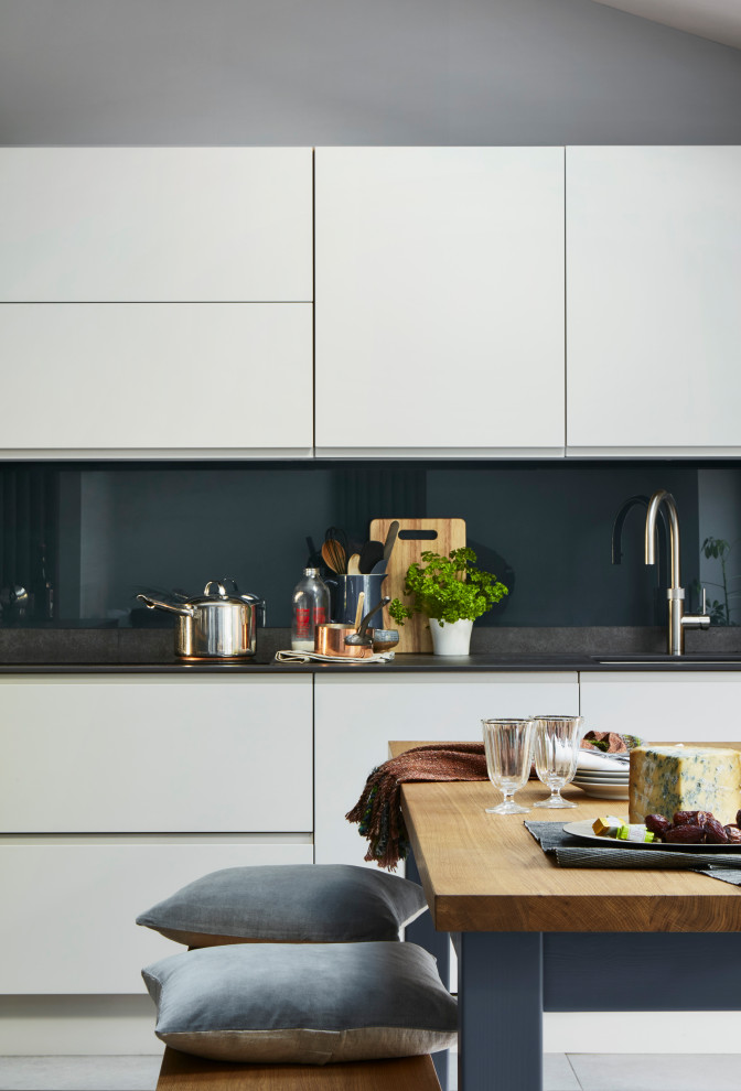 ロンドンにある高級な広いモダンスタイルのおしゃれなキッチン (青いキャビネット、青いキッチンパネル、ガラス板のキッチンパネル、パネルと同色の調理設備) の写真