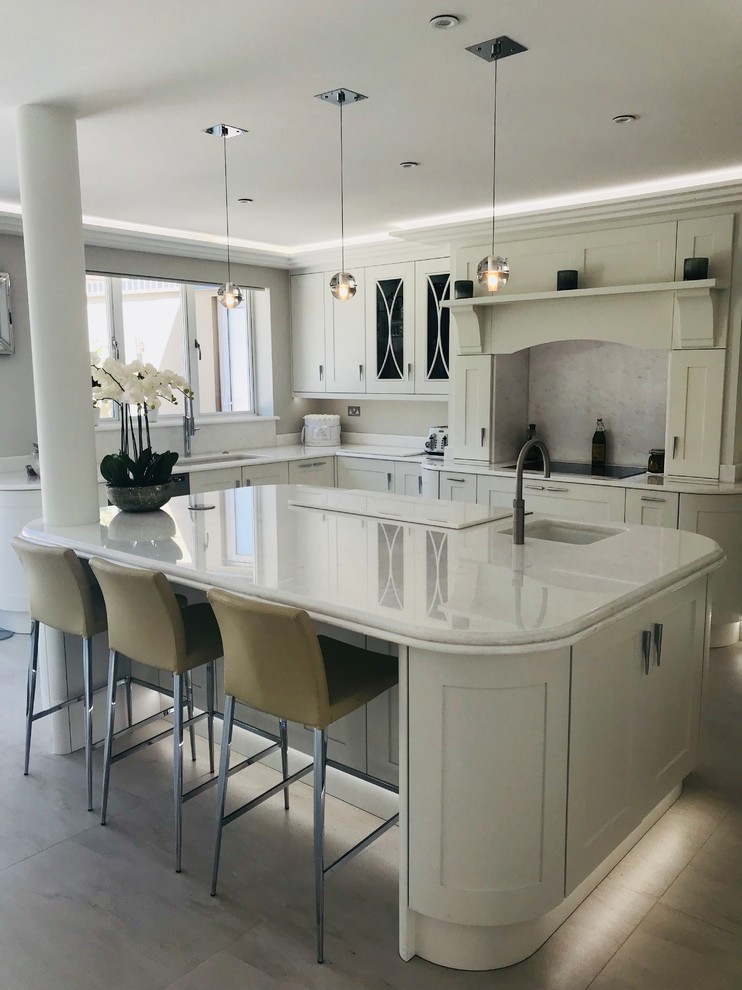 Inspiration for a large contemporary open plan kitchen in Hertfordshire with a built-in sink, shaker cabinets, white cabinets, quartz worktops, white splashback, stone slab splashback, integrated appliances, porcelain flooring, an island, white floors and white worktops.