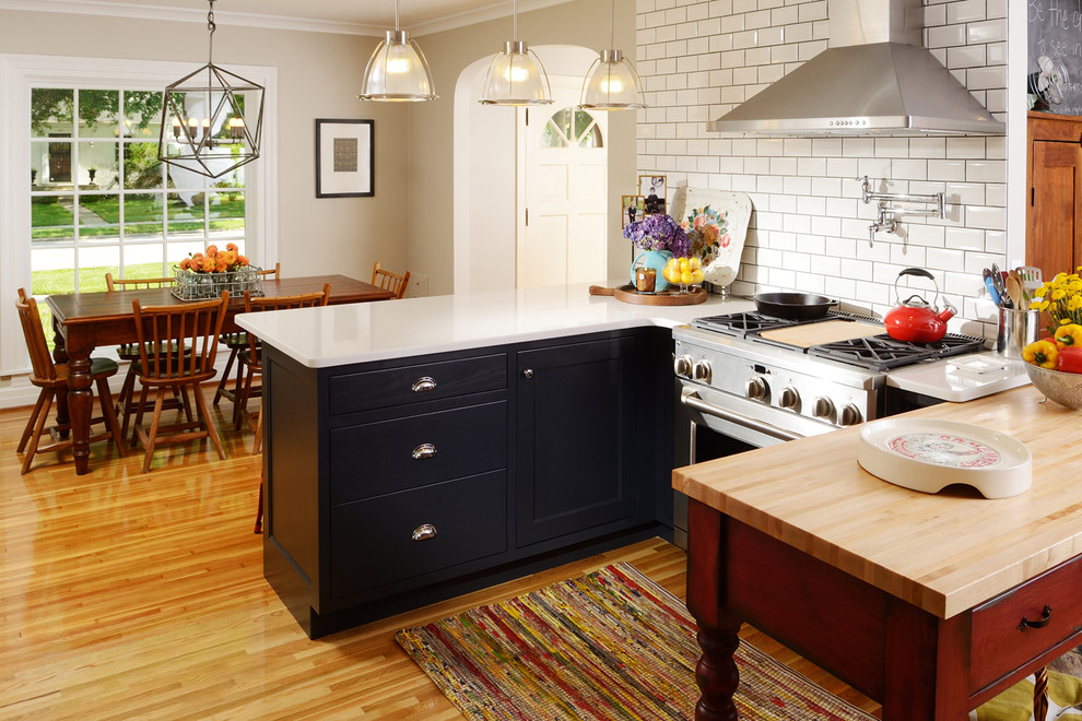Eat-in kitchen - mid-sized traditional u-shaped light wood floor eat-in kitchen idea in Other with a farmhouse sink, shaker cabinets, black cabinets, quartz countertops, white backsplash, subway tile backsplash, stainless steel appliances and a peninsula