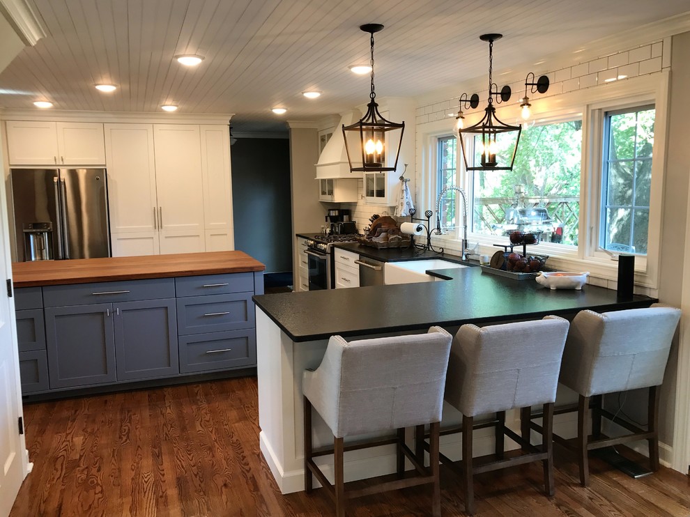 Large cottage u-shaped dark wood floor and brown floor enclosed kitchen photo in Other with a farmhouse sink, shaker cabinets, white cabinets, solid surface countertops, white backsplash, subway tile backsplash, stainless steel appliances and an island