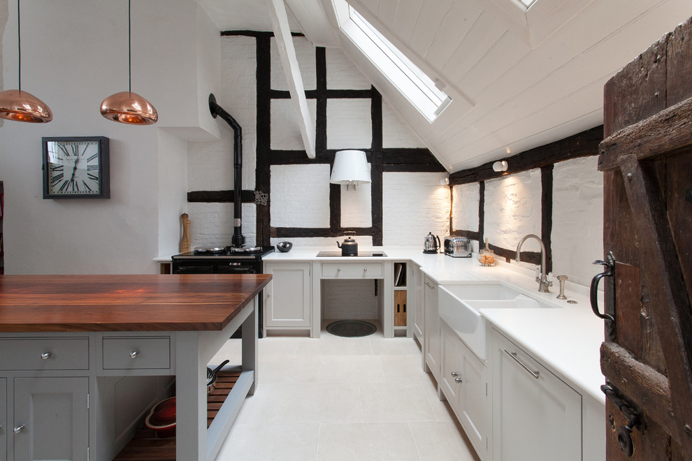 This is an example of a country kitchen in Hampshire with a belfast sink, shaker cabinets, white cabinets and an island.