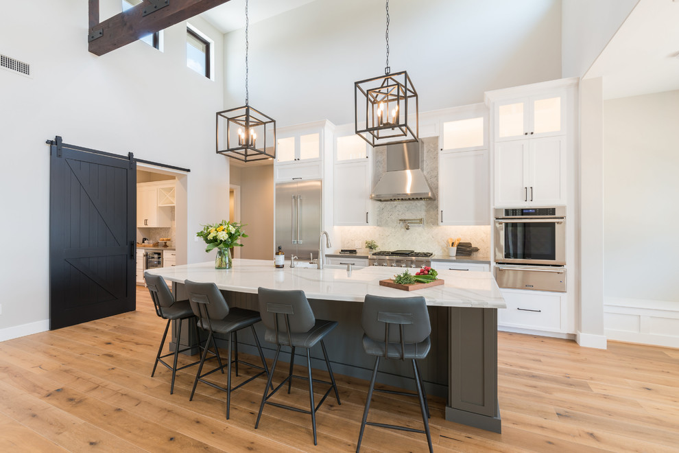 Inspiration for a mid-sized farmhouse galley light wood floor and beige floor eat-in kitchen remodel in San Luis Obispo with a farmhouse sink, recessed-panel cabinets, white cabinets, marble countertops, white backsplash, stainless steel appliances, an island, white countertops and stone tile backsplash