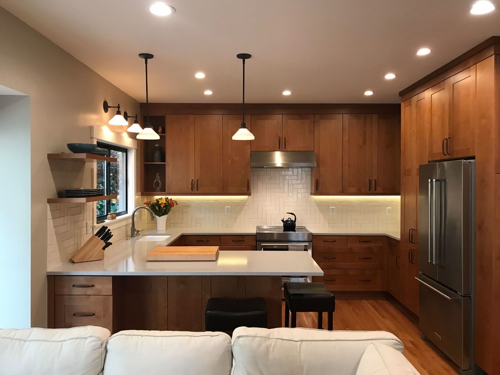 Bild på ett mellanstort amerikanskt grå grått kök, med skåp i shakerstil, skåp i mellenmörkt trä, bänkskiva i kvarts, vitt stänkskydd, stänkskydd i keramik, rostfria vitvaror, mellanmörkt trägolv, en halv köksö, brunt golv och en undermonterad diskho