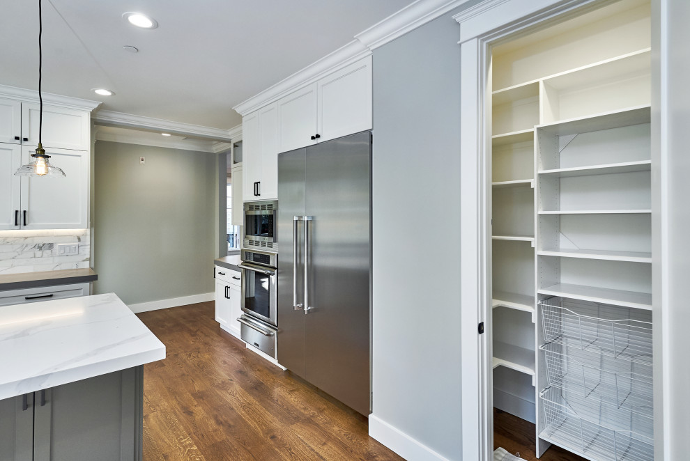Medium sized classic l-shaped kitchen pantry in San Francisco with a belfast sink, shaker cabinets, white cabinets, engineered stone countertops, grey splashback, metro tiled splashback, stainless steel appliances, medium hardwood flooring, an island, brown floors and grey worktops.