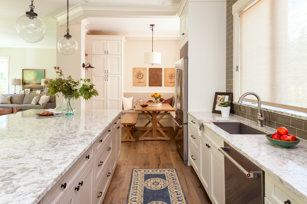 Design ideas for a large rural l-shaped open plan kitchen in Seattle with a submerged sink, shaker cabinets, white cabinets, green splashback, metro tiled splashback, stainless steel appliances, medium hardwood flooring, an island, brown floors and quartz worktops.